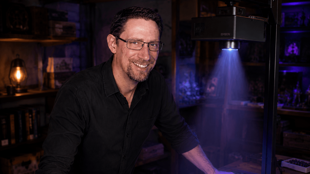 James Phillips standing beneath an overhead projector beside a tabletop projection test.